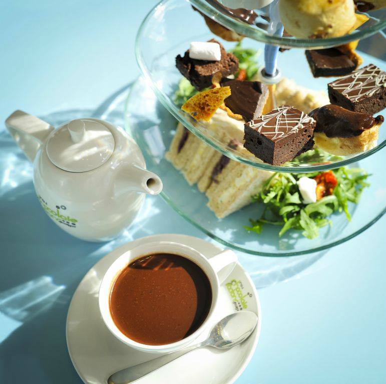 Sunlit high tea presentation with a cup of hot chocolate on a blue table cloth at the Chocolate Factory, Glasgow.