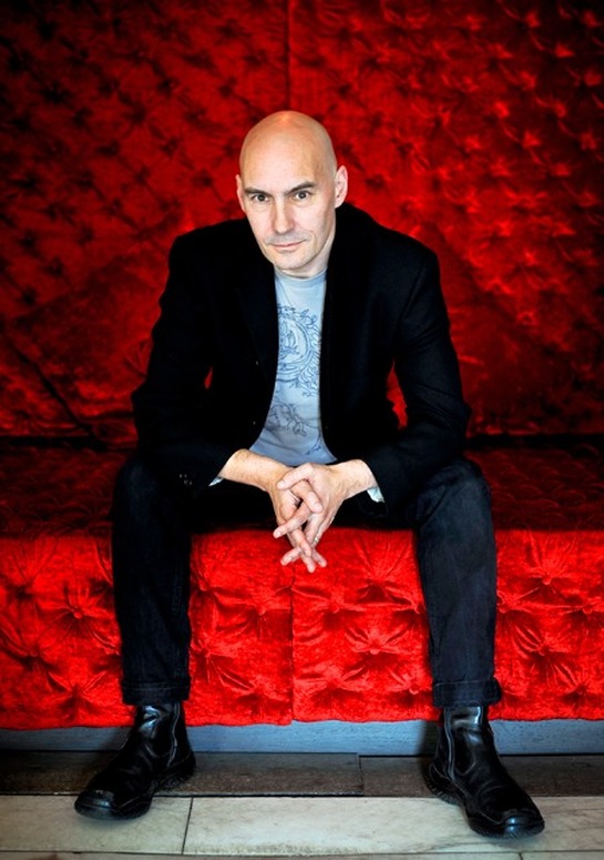 Scottish Comic Book writer and screenwriter Grant Morrison sitting on a plush red chair for a List editorial